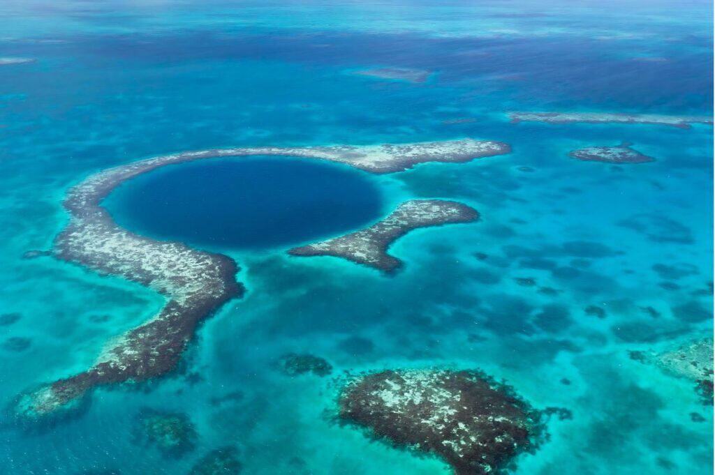 Aerial view of the Great Blue Hole, a large underwater sinkhole surrounded by turquoise ocean waters and coral reefs located off the coast of Belize.