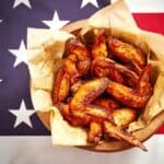 A basket of seasoned chicken wings on parchment paper sits on an American flag background.