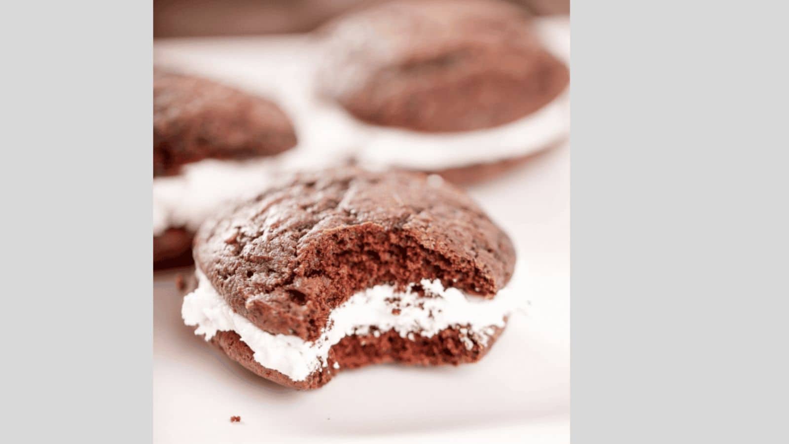 A chocolate whoopie pie with marshmallow filling with a bite out of it.