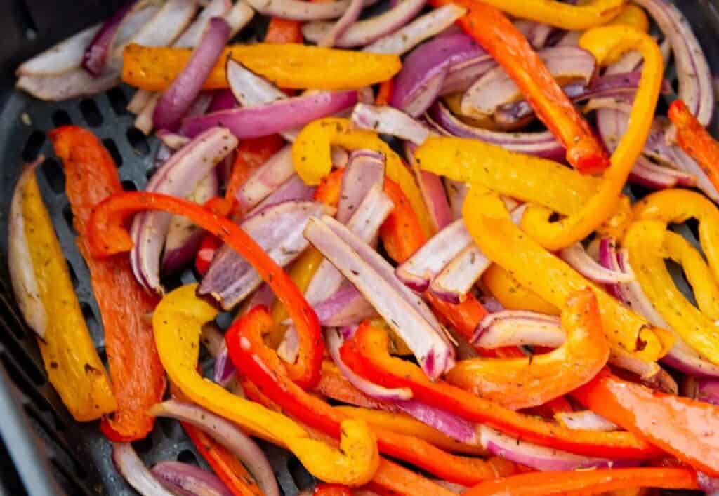 A mix of sliced red, yellow, and orange bell peppers with red onion strips, cooked in an air fryer.