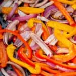 A mix of sliced red, yellow, and orange bell peppers with red onion strips, cooked in an air fryer.