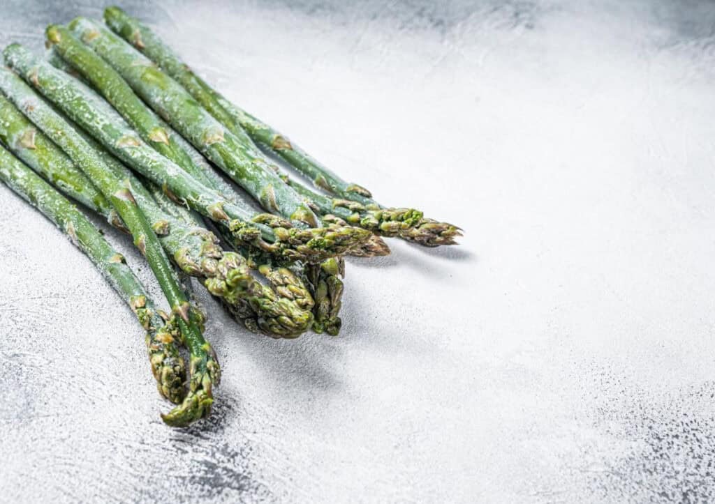 A group of raw green asparagus spears on a textured light gray surface.
