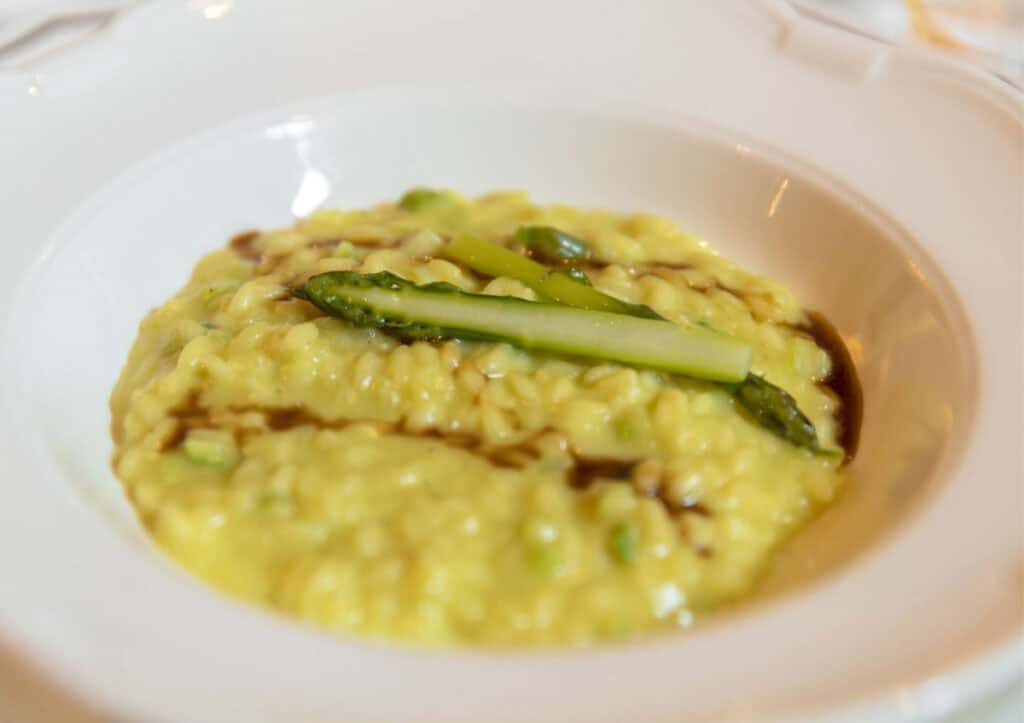 A plate of creamy risotto garnished with asparagus spears and drizzled with a dark sauce.