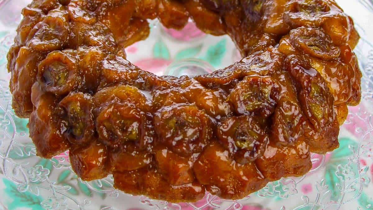 Close-up of a sticky caramel glazed monkey bread ring with small dough balls, topped with a caramelized finish, displayed on a decorative glass plate.