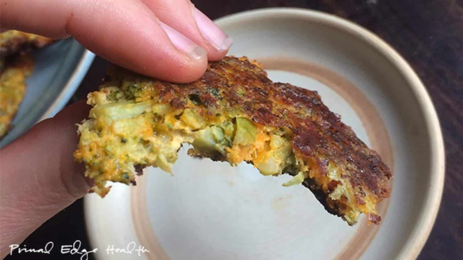 A close-up of a hand holding a partially eaten broccoli fritter over a round plate.