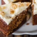 One piece of carrot cake being pulled away from the rest of the cake with a silver spatula.