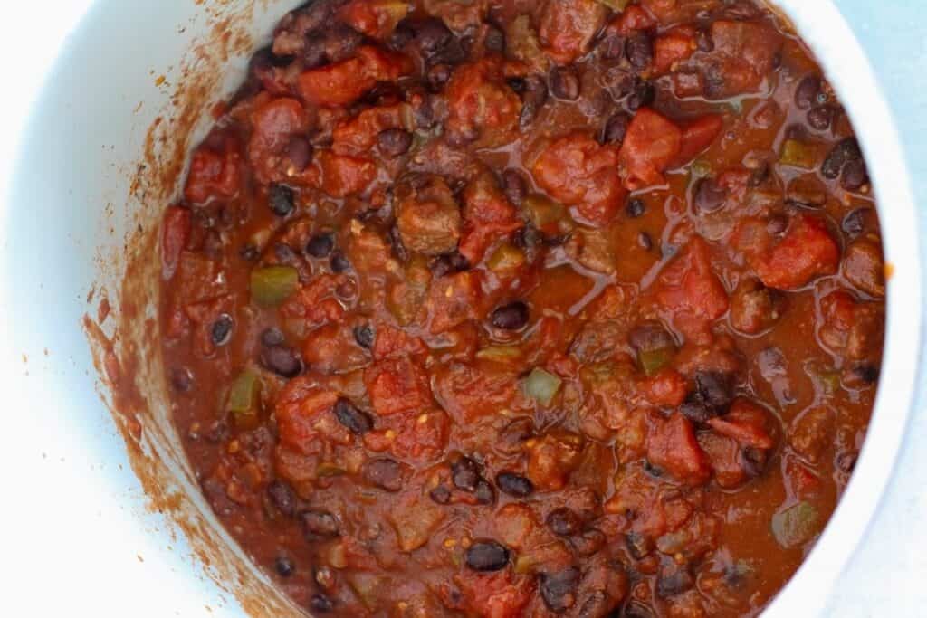 A pot filled with cooked chili containing black beans, diced tomatoes, bell peppers, and ground meat.