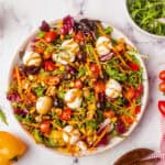 A rainbow salad with lettuce, tomatoes, carrots, olives, corn, and mozzarella balls is drizzled with dressing.