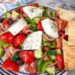 Horiatiki Salad with feta cheese on top served on a plate.