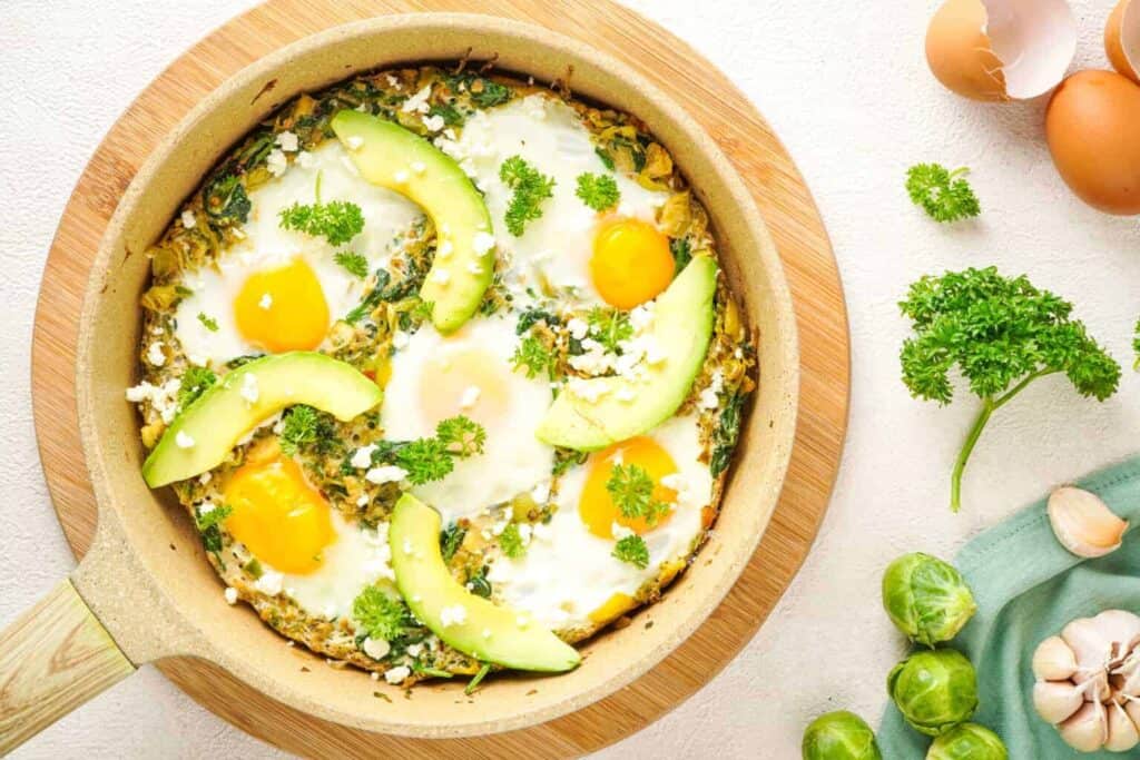 Eggs and avocados in a skillet with herbs on the site.