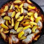 A cast iron skillet filled with cooked chicken pieces and topped with sliced peaches.