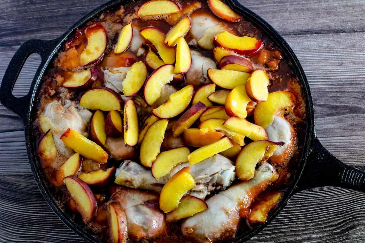 A cast iron skillet filled with cooked chicken pieces and topped with sliced peaches.