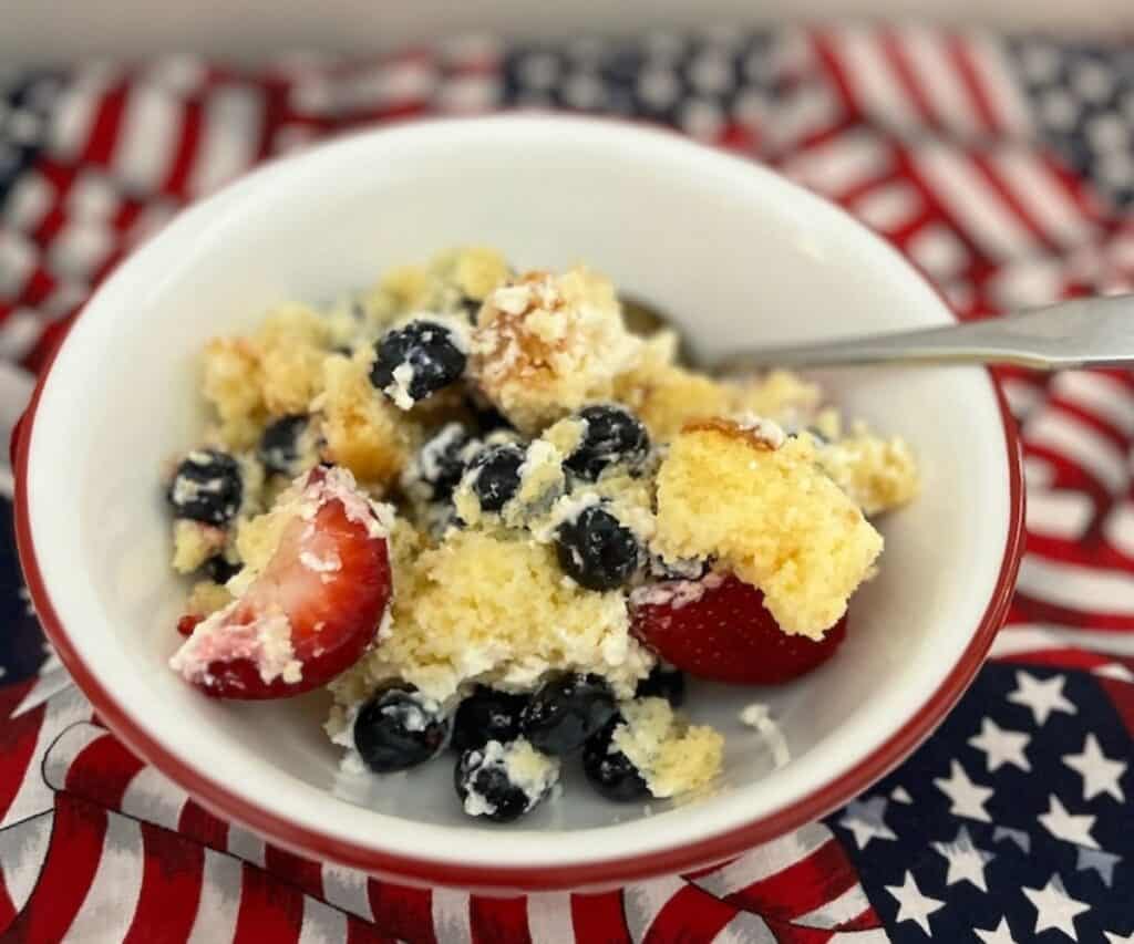 A bowl of cake topped with blueberries and strawberries, served on a flag-themed cloth.