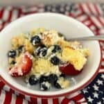 A bowl of cake topped with blueberries and strawberries, served on a flag-themed cloth.