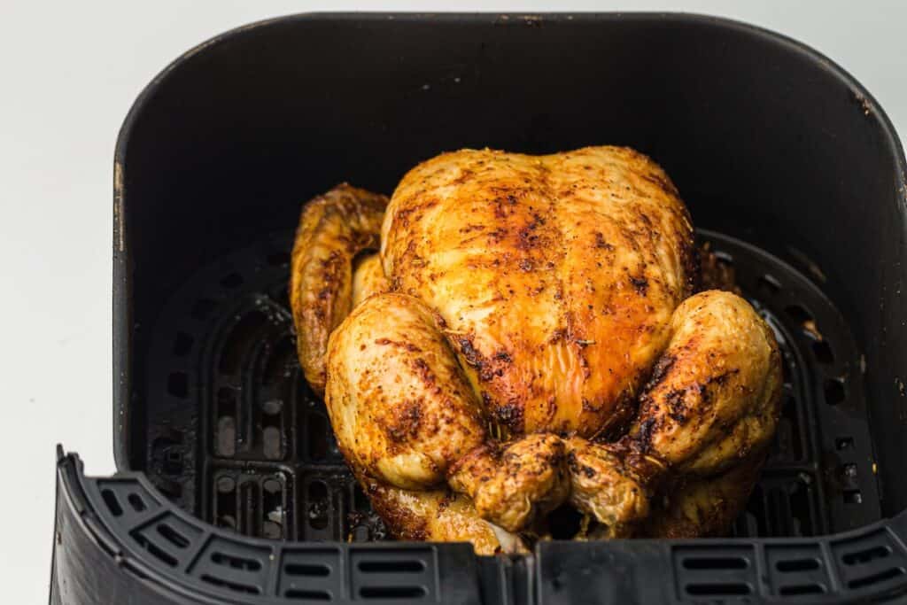 Whole roasted chicken seasoned and cooked to golden brown perfection in an air fryer basket.