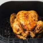 Whole roasted chicken seasoned and cooked to golden brown perfection in an air fryer basket.