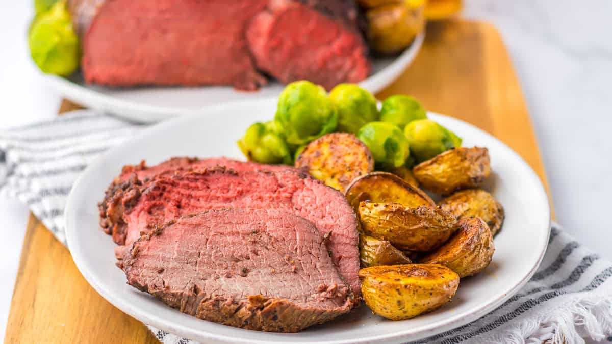 A plate with four slices of roast beef, some roasted potatoes, and Brussels sprouts.
