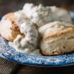 A blue and white plate with a biscuit covered in white sausage gravy, a classic example of southern food. The plate is set on a wooden surface.