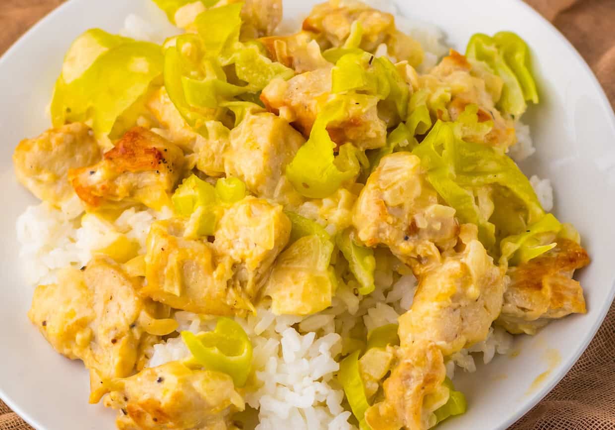 A plate of white rice topped with chunks of chicken and sliced green bell peppers, all cooked in a creamy yellow sauce.