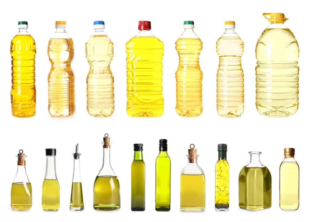 A row of plastic bottles and a row of glass bottles, all filled with various types of cooking oil in different shades of yellow and amber.