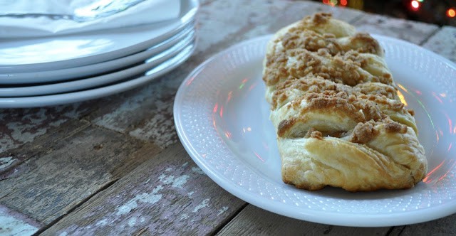 A plate with a braided pastry sits on a wooden table beside a stack of plates and a napkin.