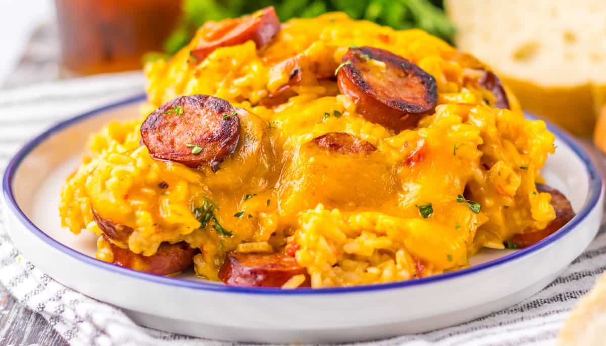 A close-up of a plate of cheesy sausage jambalaya, featuring sliced sausage, melted cheese, and rice, garnished with herbs.