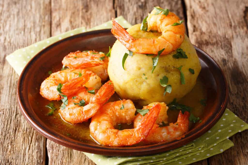 A plate of delicious Caribbean food, mofongo garnished with shrimp and parsley, placed on a wooden surface with a green polka dot napkin.