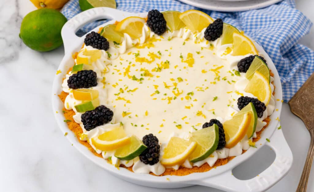 A pie topped with whipped cream, blackberries, lime slices, and lemon slices.