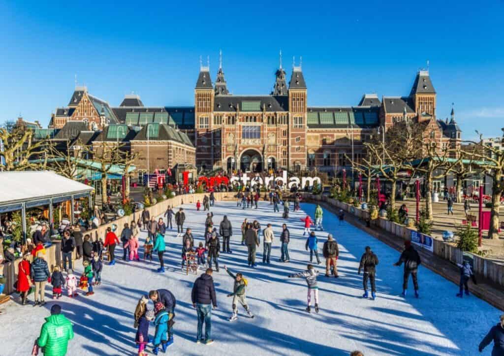 A group of people ice skating on a rectangular rink in front of a castle-like building.