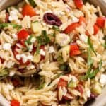 A bowl of orzo pasta salad with chopped tomatoes, olives, cucumbers, red onions, basil, and crumbled feta cheese.