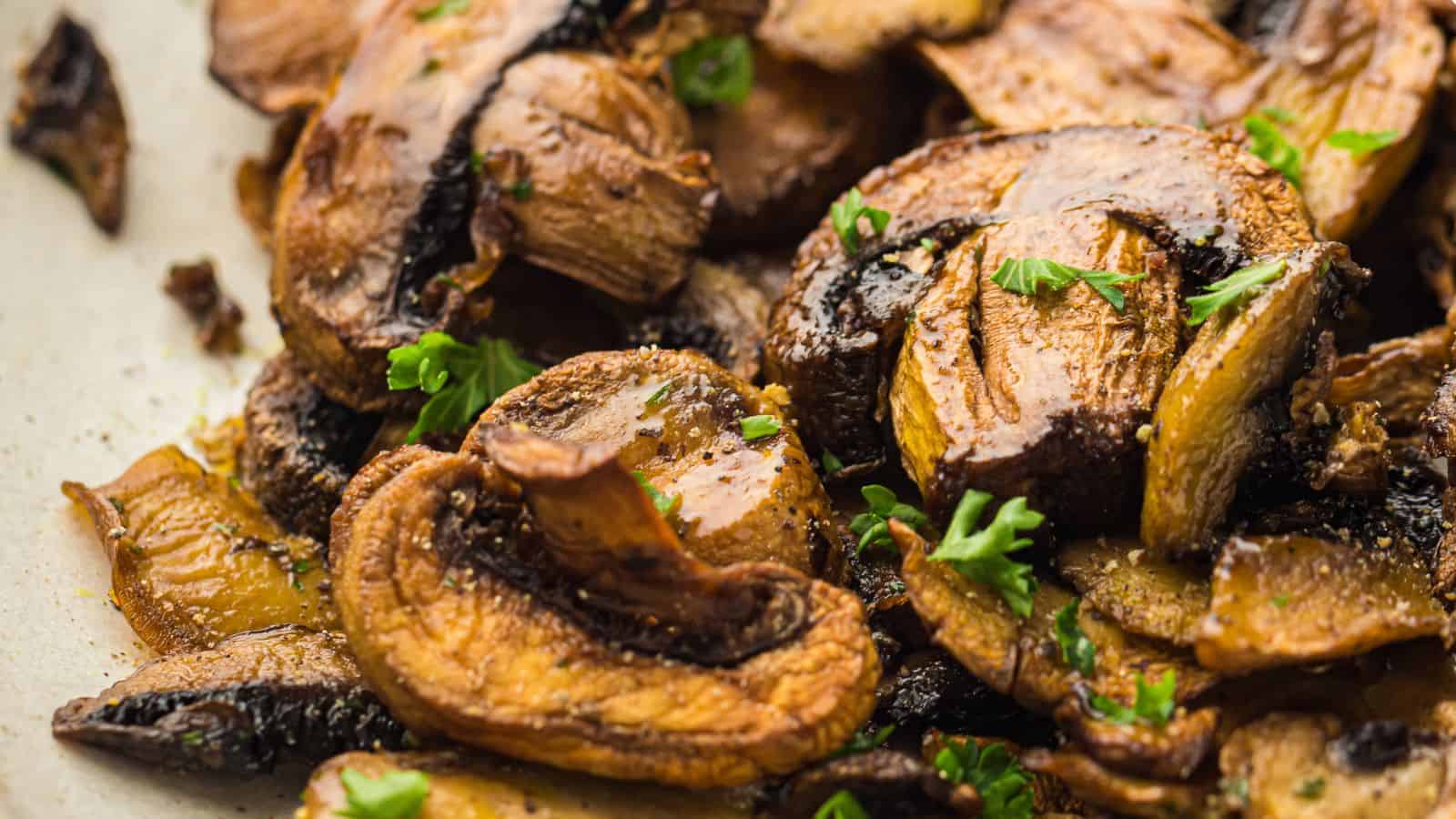 Close-up of golden-brown air fryer mushrooms garnished with chopped parsley. The mushrooms appear perfectly cooked to a tender texture.