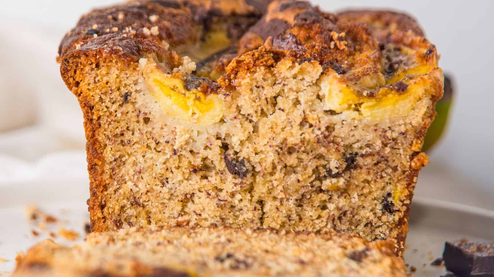 Close-up view of a sliced banana bread loaf with visible chunks of banana and nuts on a white plate.