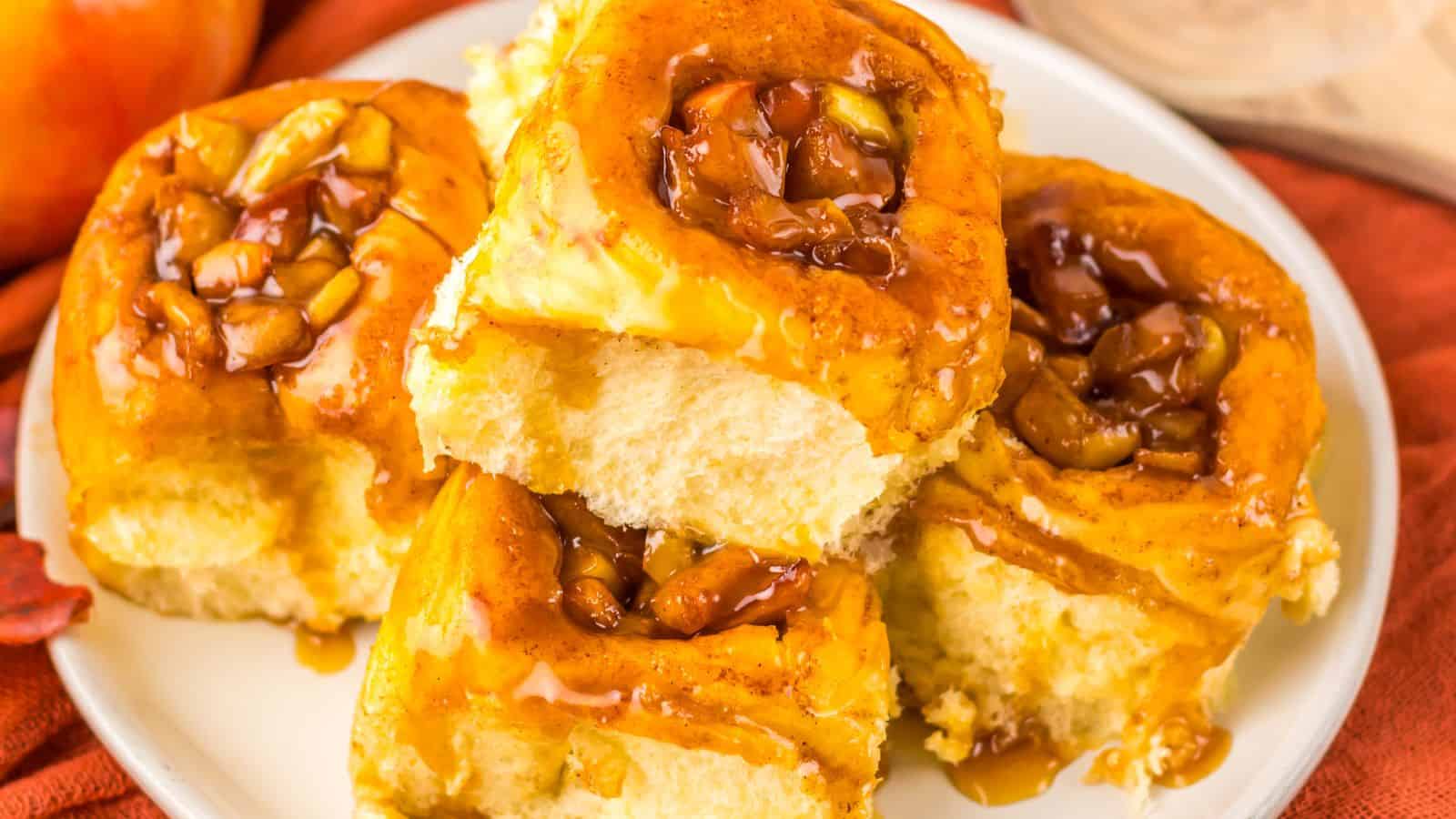 A plate of five sticky buns topped with caramelized nuts and sauce, resting on a red cloth.