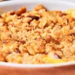 Close-up of a baked dish with a golden-brown crumb topping, possibly a dessert like an apple crisp or a cobbler, in a round white baking dish.