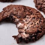 A close-up of a partially eaten chocolate cookie with a gooey center resting on a white surface.