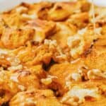 A close-up of bread pudding with nuts, drizzled with caramel sauce in a white dish.