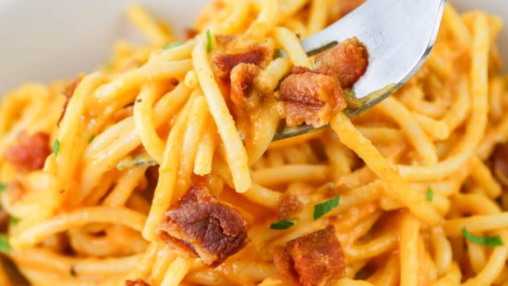 Close-up of a forkful of spaghetti carbonara garnished with crispy bacon bits and parsley.