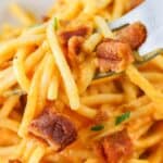 Close-up of a forkful of spaghetti carbonara garnished with crispy bacon bits and parsley.