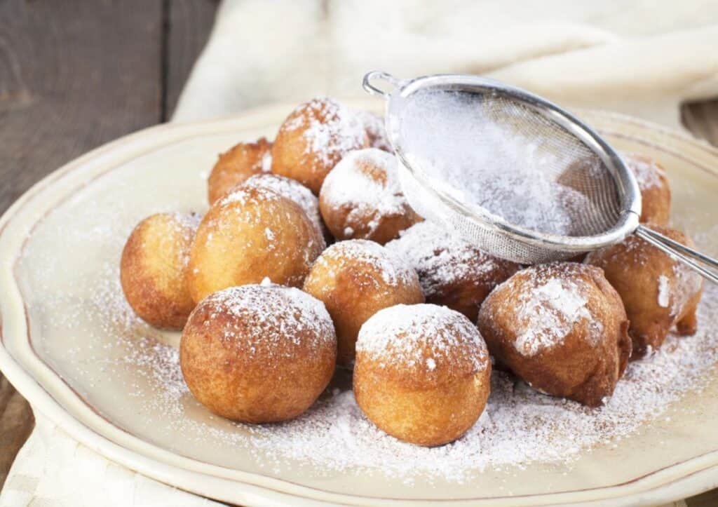 A plate of fried dough balls on a white plate sprinkled with powdered sugar.