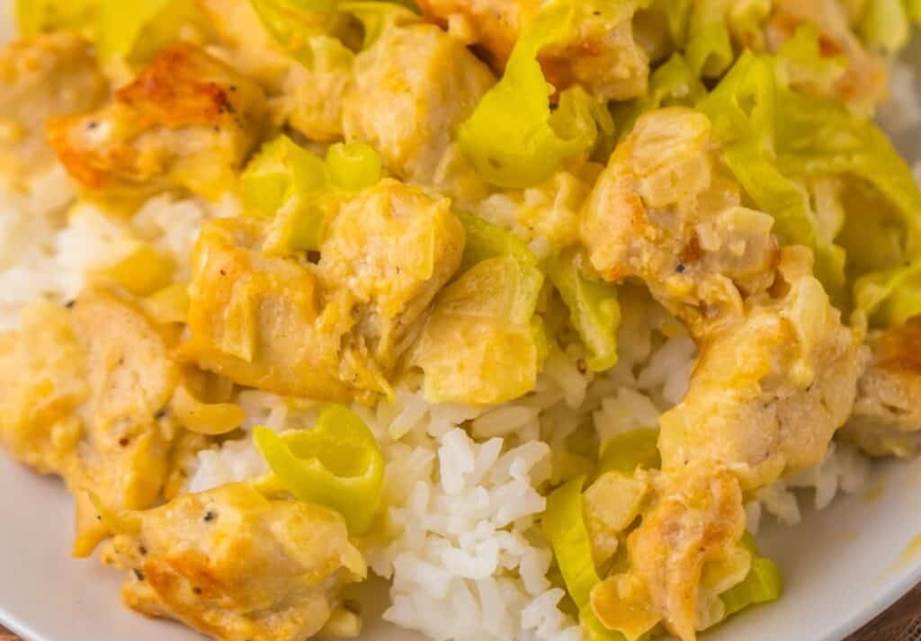 A plate of white rice topped with chunks of chicken, yellow bell pepper rings, and a creamy sauce.