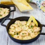 Shrimp scampi with a slice of lemon on a black dish.