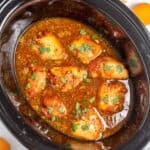 Slow cooker filled with apricot chicken garnished with chopped cilantro, with fresh apricots and cilantro on the side.