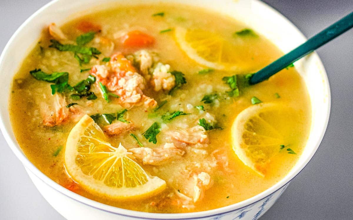 A bowl of soup with chunks of chicken, rice, and vegetables, garnished with lemon slices and fresh herbs.