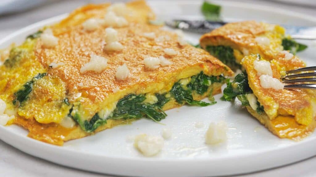 A spinach and cheese omelette is partially sliced on a white plate. 