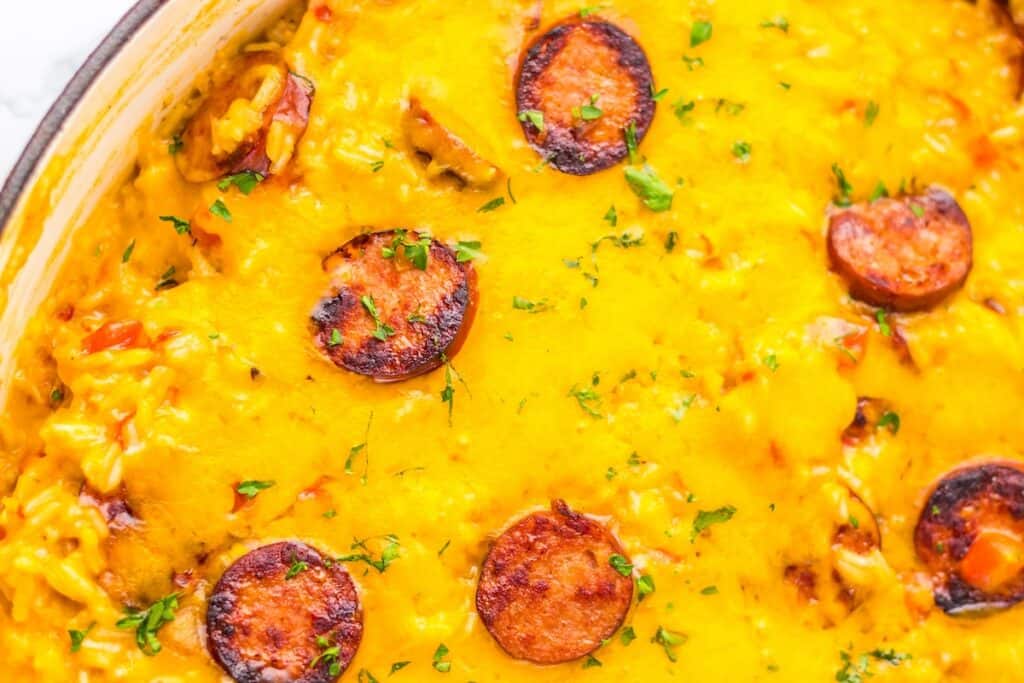 A close-up of a baked dish topped with melted cheese, slices of sausage, and garnished with chopped herbs.