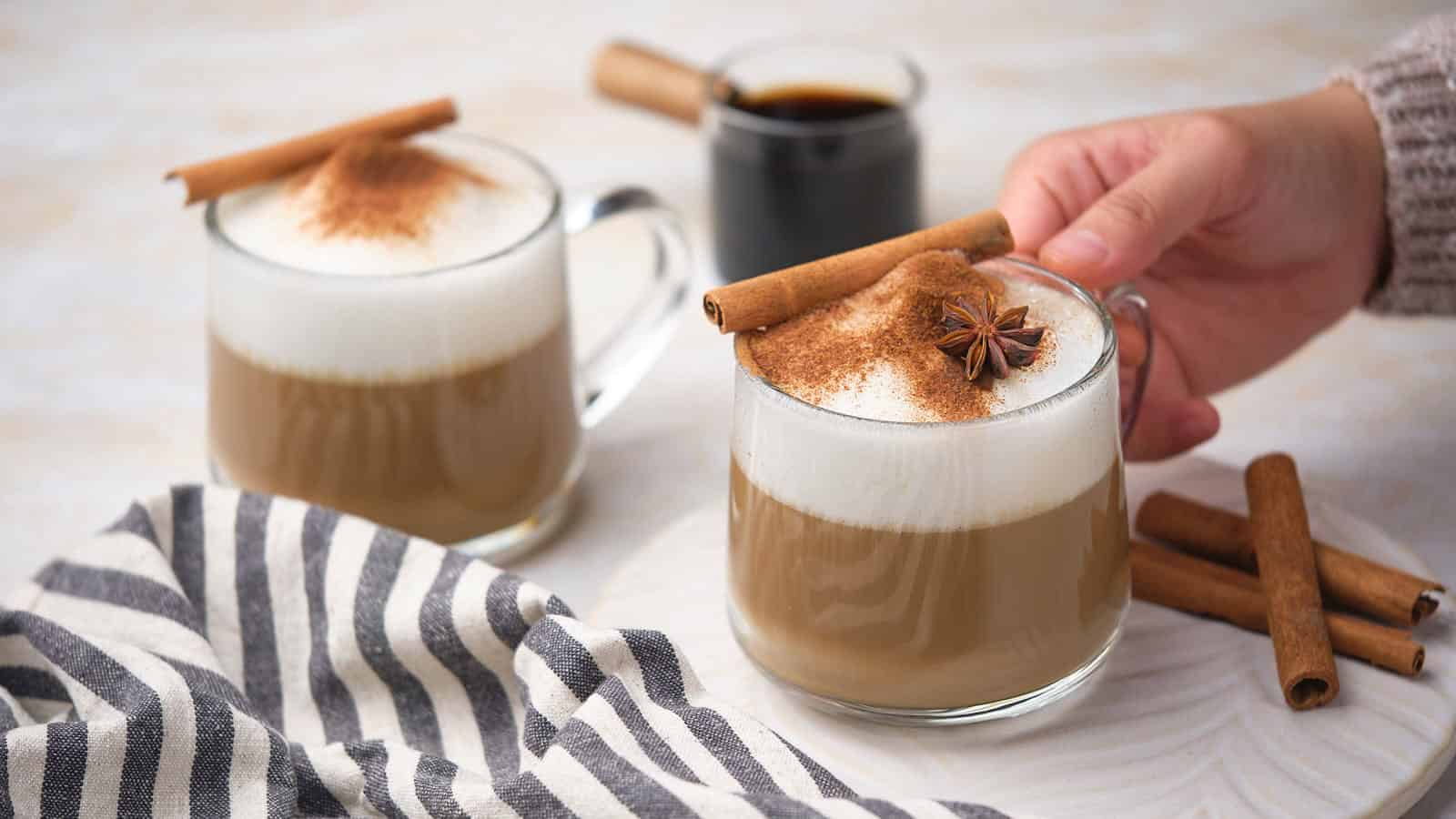 Two glass mugs of dirty chai tea latte, with one being held by a hand.