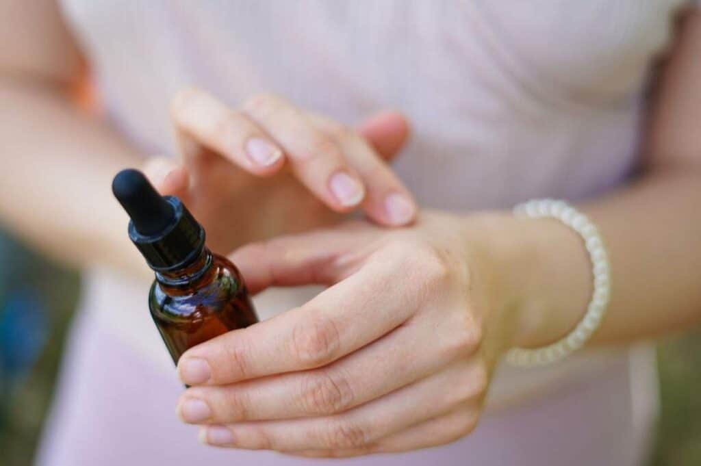 A person applies liquid from an amber dropper bottle containing essential oils for bug bites onto their wrist.