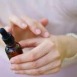 A person applies liquid from an amber dropper bottle containing essential oils for bug bites onto their wrist.