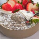 A bowl of chia pudding topped with sliced strawberries and a dollop of whipped cream, with a spoon lifting a portion.