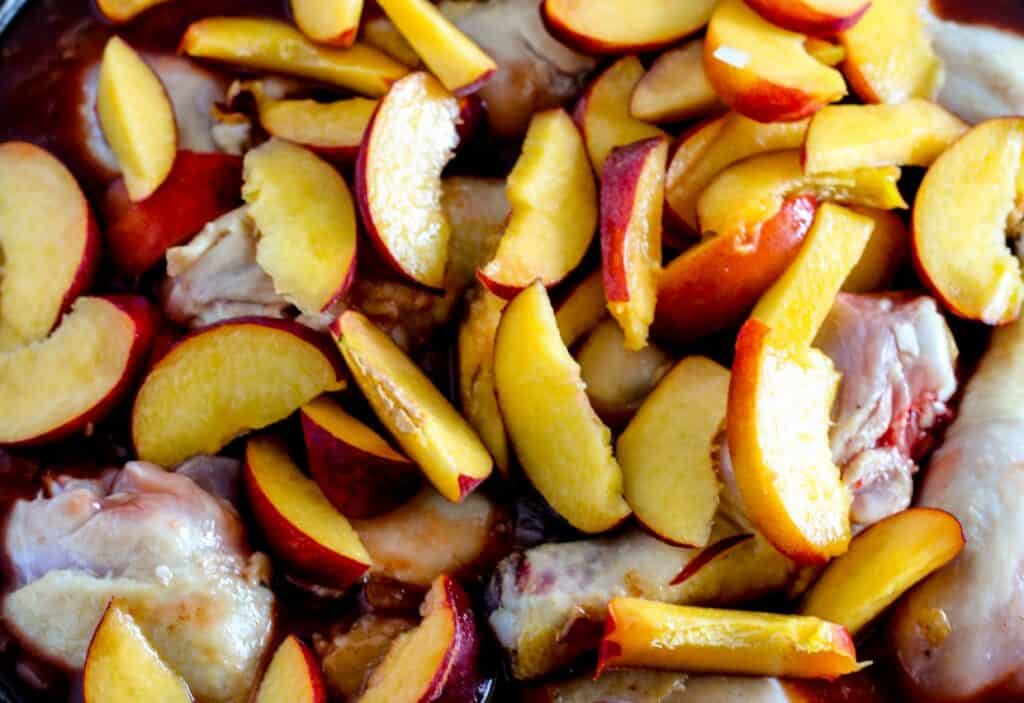 Close-up image of raw chicken pieces topped with sliced peaches, ready for cooking.